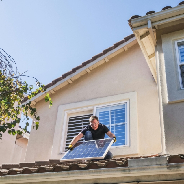 A worker installs a solar panel on a residential rooftop, showcasing renewable energy technology.